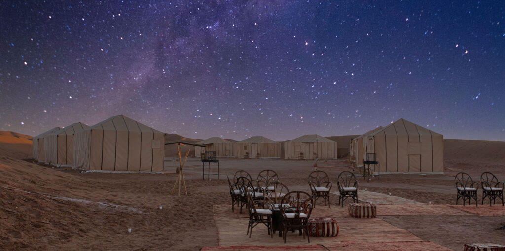A panoramic view of Chegaga Desert Camps against a backdrop of golden sand dunes.